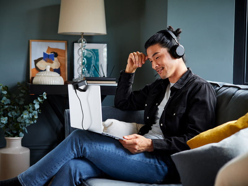 一个人戴着耳机，盘腿坐在沙发上，膝上放着一台笔记本电脑，坐在舒适的客厅里。