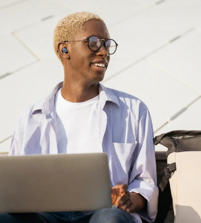 Person wearing Elite 4 earbuds while sitting on a public bench with laptop