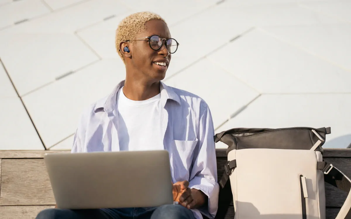 Person wearing Elite 4 earbuds while sitting on a public bench with laptop